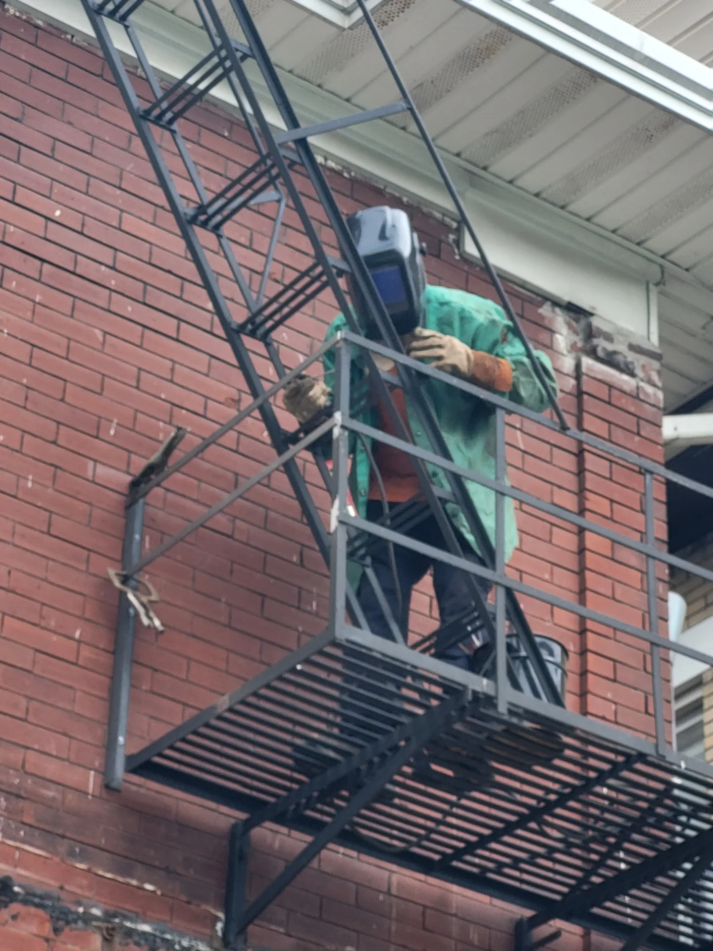 CinStar welder in full gear welding a steel fire escape on a brick building, on-site mobile service