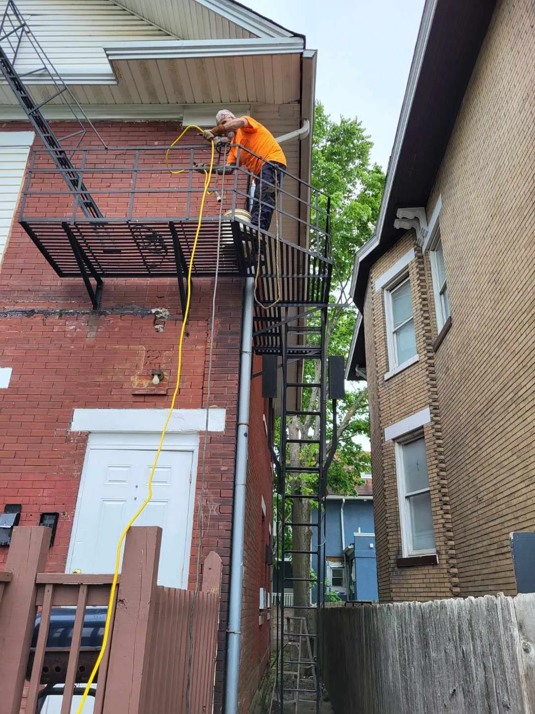 CinStar welder repairing the railing and platform of a steel fire escape on a brick apartment building