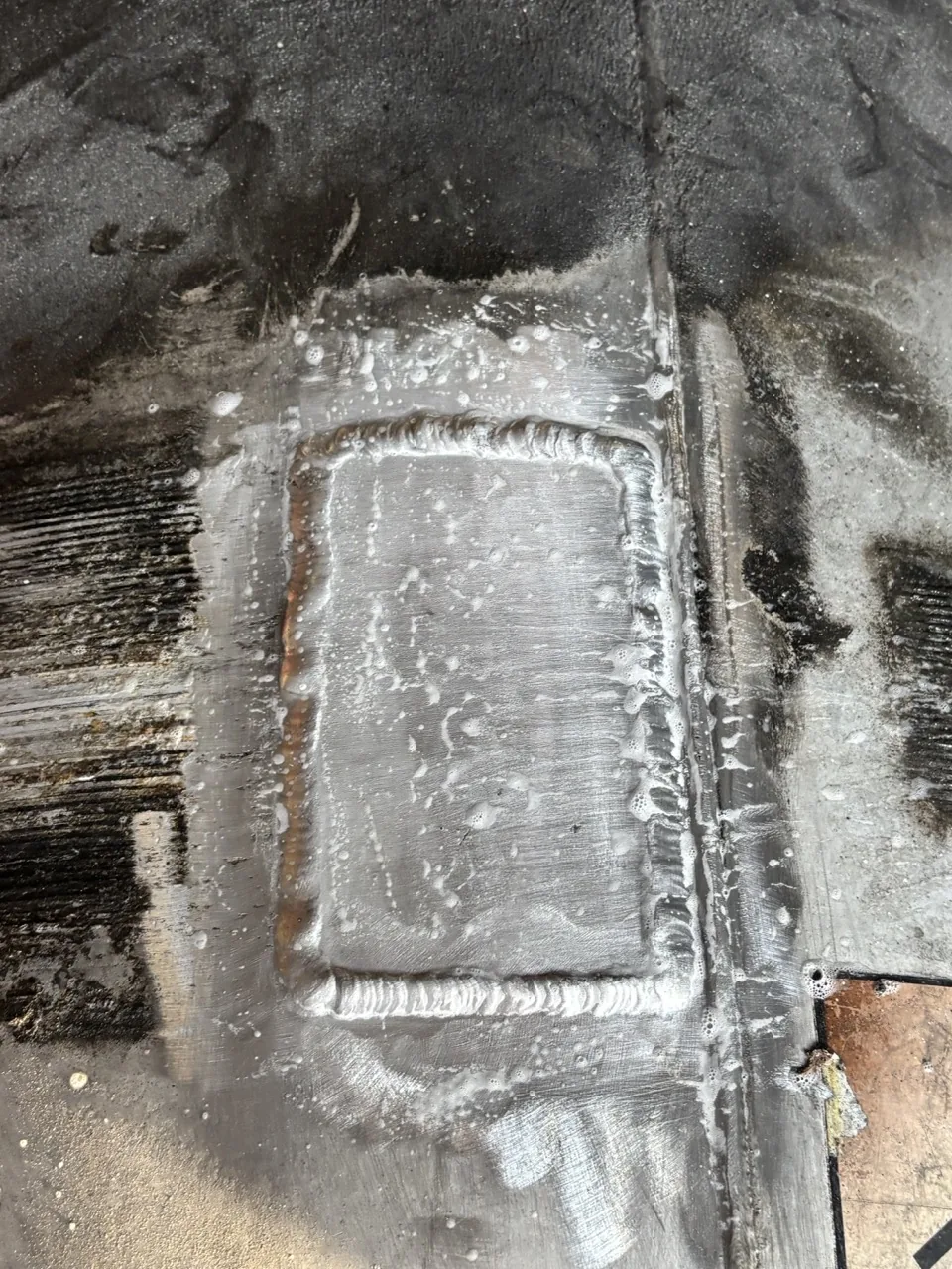 Detail of a welded aluminum fuel tank patch during a soap-bubble leak test at CinStar
