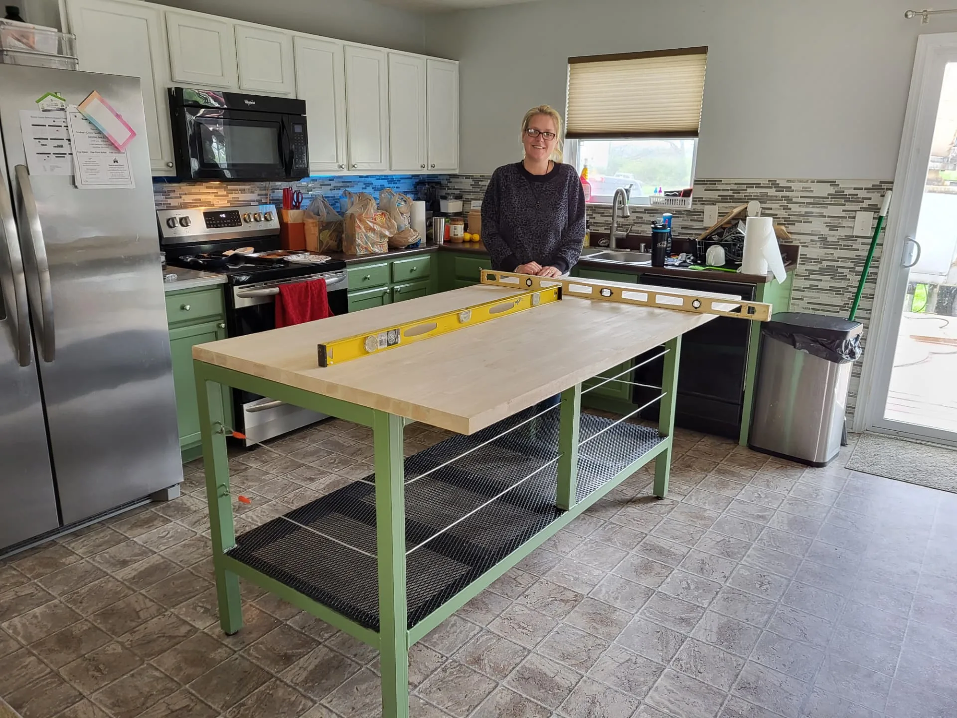 Customer standing behind her new sage green steel kitchen island with expanded metal shelving and butcher block top