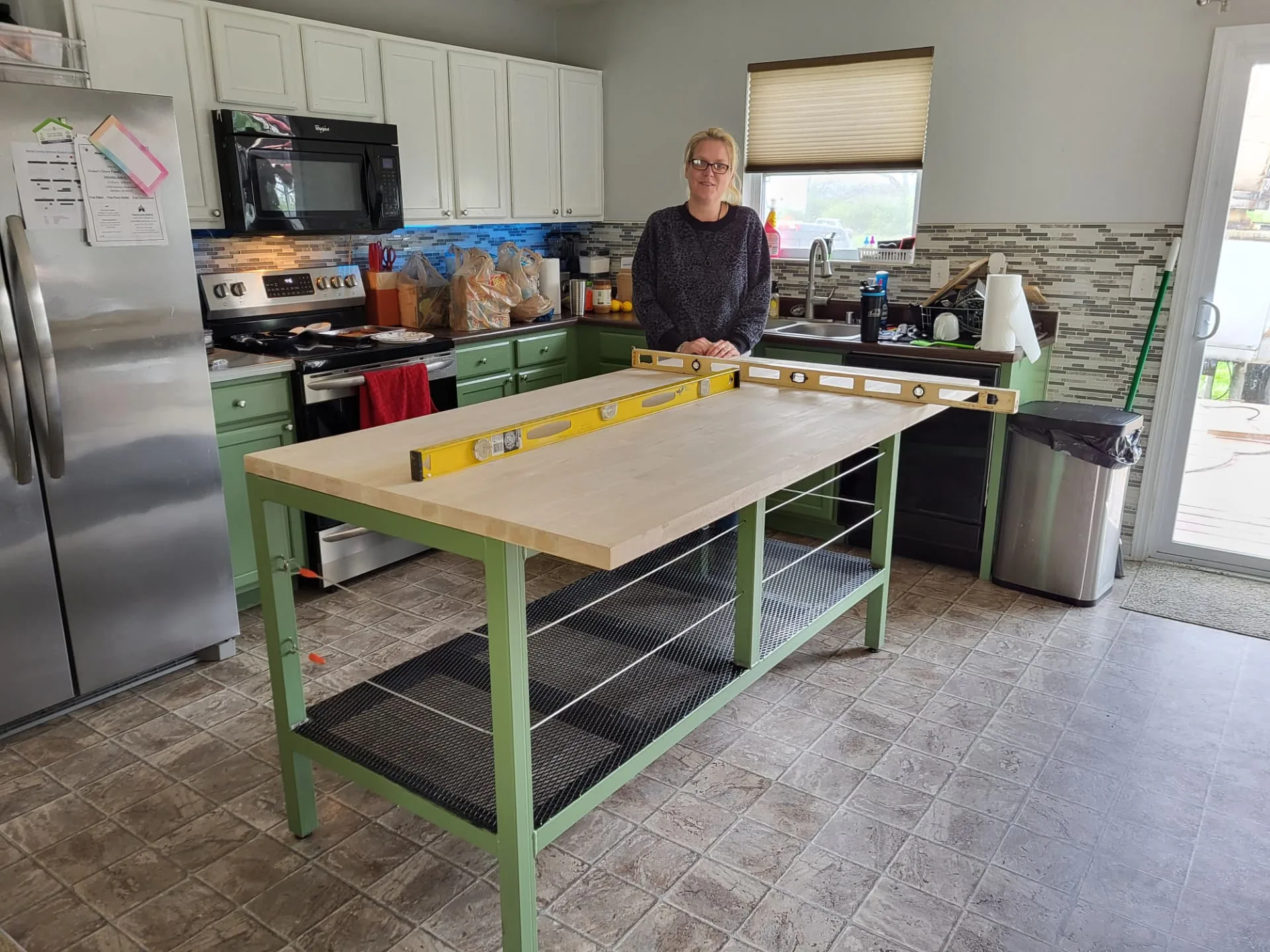 Finished sage green CinStar kitchen island base installed in the customer's kitchen with a butcher block countertop and leveling tools on top