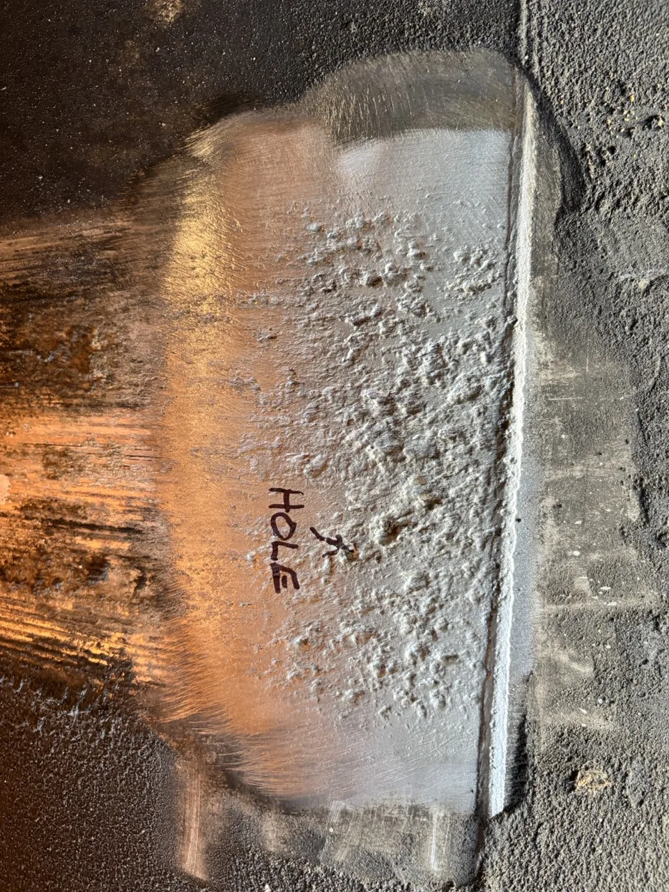 Close-up of a pinhole leak in a ground aluminum fuel tank, marked with an arrow before repair at CinStar